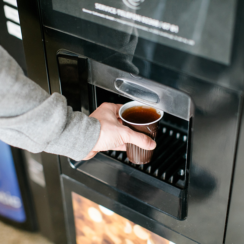 Person entnimmt Heißgetränk aus dem Getränkeautomaten