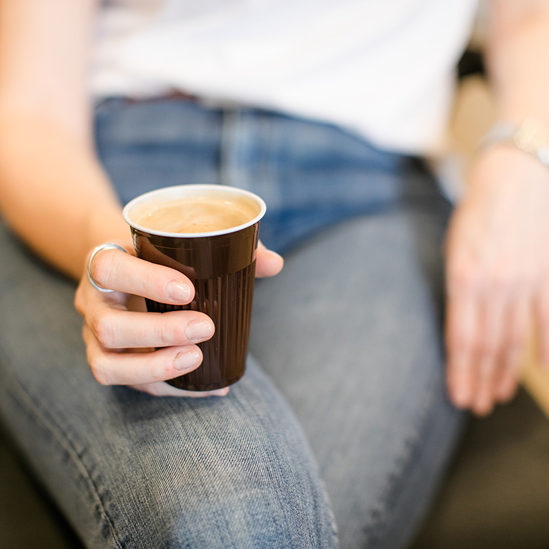 Person hält Kaffeebecher mit Kaffee in der Hand